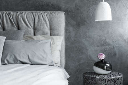 Close-up of one side of gray bed, white pendant lamp and textured wall in the backgroundの写真素材