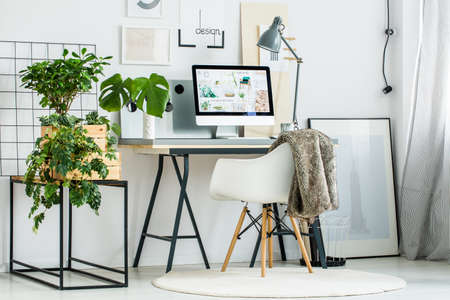 Modern office room with designed chair on white carpet and grey lamp on desk