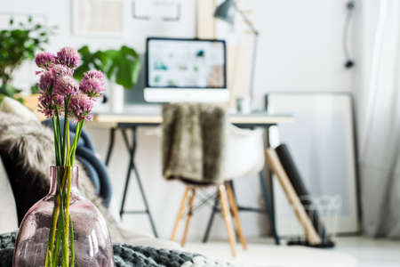 Violet flowers in glass vase in simple office room with picture on floor