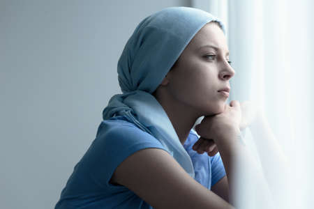 Breast cancer survivor in a blue scarf resting chin on her handsの写真素材