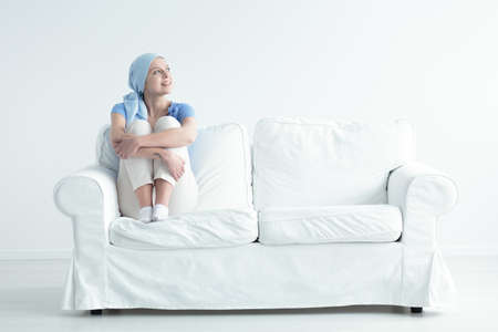 Happy cancer patient feeling relieved and holding her knees on a white sofaの写真素材