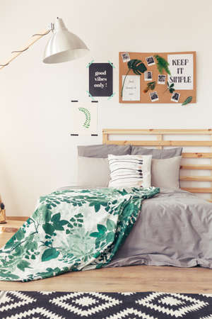 Close-up view of bedroom in natural design with white wall, lamp, posters, photos, rug, wooden floor...