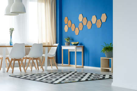 Contemporary stylish dining room with blue wall, wooden table, white chairs, patterned rug, window and corkの写真素材