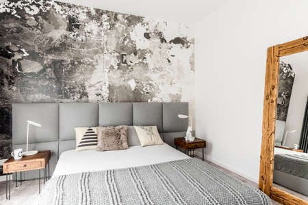 Gray and white interior of modern bedroom with wooden bedside table, big rustic mirror and abstract grunge wall decorの写真素材