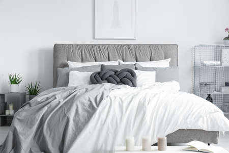 Handmade dark pillow on the big bed placed under minimalistic posterの写真素材