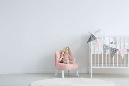 Roomy children's bedroom with a white, circular carpet, a pink chic chair with a toy sitting on it, and a baby bedの写真素材