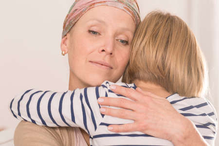 Sick mother with brain tumor tightly hugging her little childの写真素材