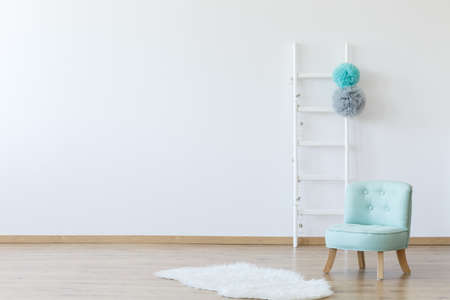 Elegant interior of children's room with a decorated ladder, a mint comfortable chic chair, and a fake animal skin lying on the wooden floor