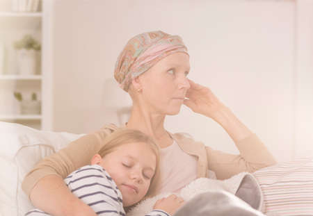 Ill mother with headscarf after chemotherapy embracing her sleeping childの写真素材