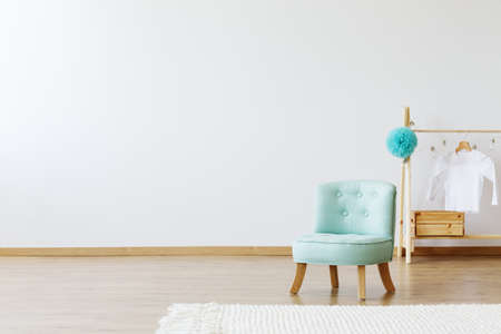 Scandinavian style kid's room interior with a pastel mint chic chair next to a clothes stand with a white t-shirtの写真素材
