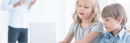 Blonde haired siblings looking at laptop screen with interest