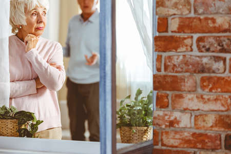 Older lady standing by the window ignoring her husband during an argumentの写真素材