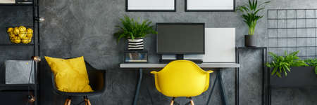 Black and yellow chair next to desk with desktop in dark roomの写真素材