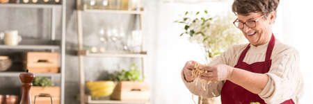 Lovely, smiling grandma preparing tasty, homemade pasta in cozy kitchenの写真素材