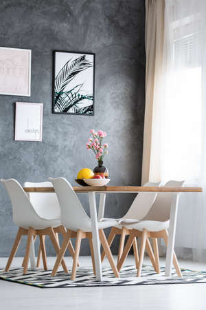 Exotic fruits in black and white bowl and pink flowers in decorative vase on dining table