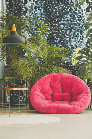 Room full of exotic plants with pink armchair and metal tableの写真素材