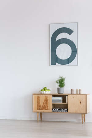 Wooden cupboard with books and simple painting on white wall in bright minimalist roomの写真素材