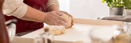 Elderly woman kneading dough in a bright kitchenの写真素材