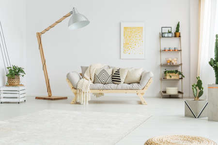 Beige coverlet lying on grey sofa with patterned pillows in bright living roomの写真素材