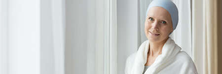 Smiling young woman with cancer standing by the windowの写真素材