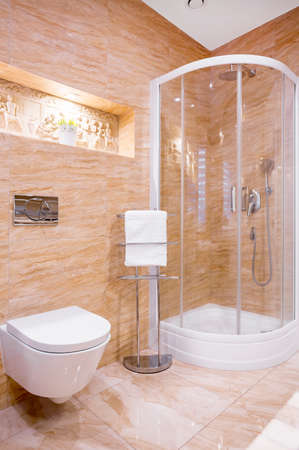 Shower in modern bathroom with beige marble and sculpture on wall