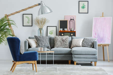 Patterned pillows on grey couch set in living room with vintage furnishings and pink painting on easelの写真素材