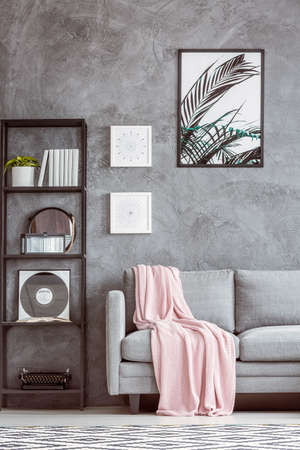 Typewriter and vinyl on shelf next to grey sofa with pink coverlet against concrete wall with posterの写真素材