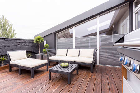 Side view of grill on stylish terrace with wooden board floor and bright garden furniture