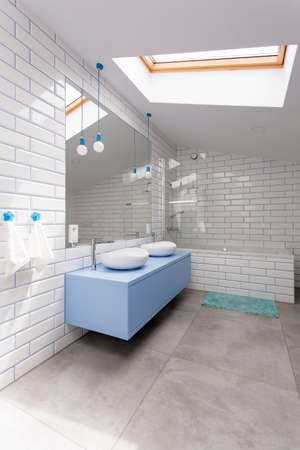 Blue washbasin cabinet and mirror in simple bathroom with glossy white brick wallの写真素材