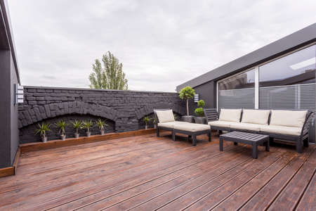 Plants and beige garden furniture on terrace with wooden floor and black brick wallの写真素材