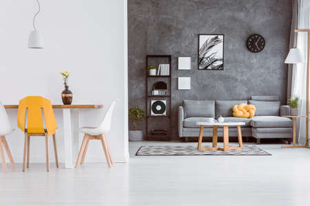Decorative vase on dining table with yellow chair in living room with grey settee against dark wall