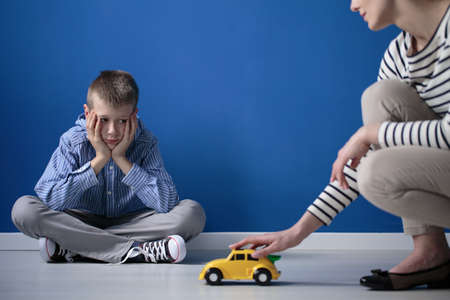 Kid is looking on yellow toy car while sitting with crossed legs on white floorの写真素材