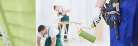 Man with green paint roller and tools, carpenter in backgroundの写真素材