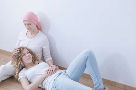 Daughter lying head on lap of sick mother suffering from cancerの写真素材