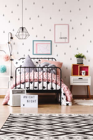 Plant in striped pot on bedside cabinet next to bed with knit pink blanket in pastel kids room