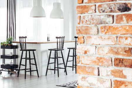 Red brick wall in rustic dining room with white lamps above countertop with black bar stoolsの写真素材