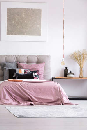 Decorative vases on table in stylish bedroom with copper plate and pink bedsheets on king-size bedの写真素材