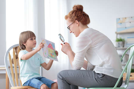 Adoptions counselor looking via magnifying glass on a picture of perfect home shown by an orphan boyの写真素材