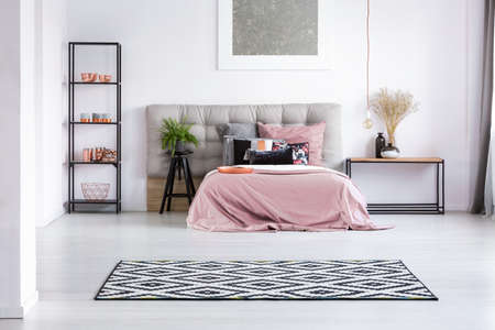 Black and white geometric carpet in bedroom with copper elements and king-size bed with pink overlayの写真素材