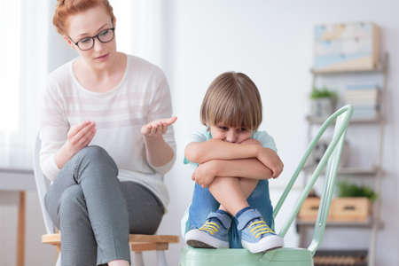 Worried autistic boy sitting with crossed legs on mint chair during conversation with psychiatrist