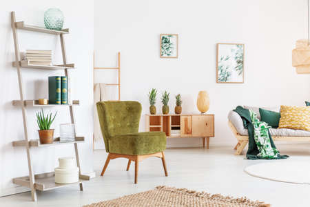Pear green chair and yellow pillow on beige sofa in cozy room with accessories on wooden shelfの写真素材