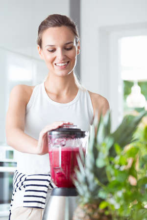 Healthy woman standing in kitchen and mixing beet smoothie in blender for fresh breakfastのeditorial素材