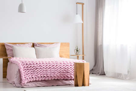 A wooden table and lamp stands next to king-size bed with pink overlayの写真素材