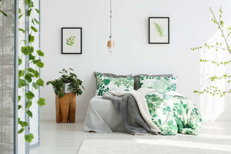 Plant on wooden designer table next to king-size bed with floral bedding in green bedroom with handmade lampの写真素材
