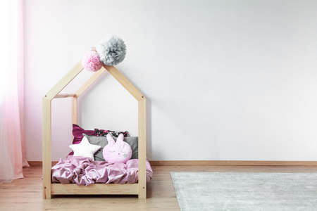 Tulle pompons on wooden kids bed with pink satin bedding and creative pillows in spacious bedroomの写真素材