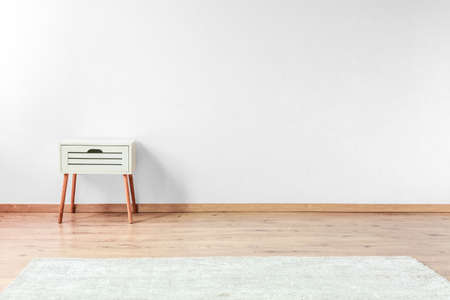 White bedside cabinet on wooden floor in open space with white carpet and white wallの写真素材