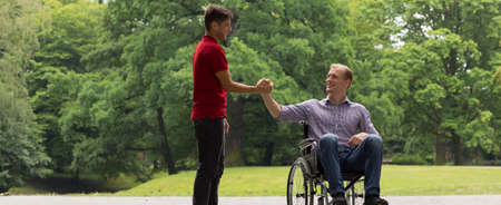 Disabled man greeting with friend in the parkの写真素材