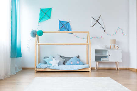 Small lamp on cupboard next to bed with star shaped pillows on blue bedding in boys bedroom with DIY kites on white wallの写真素材