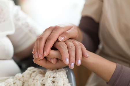 Close-up photo of a female caregiver and senior woman holding hands. Senior care concept.の写真素材