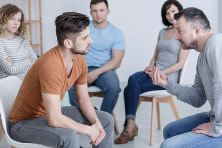 Psychologist talking to young man in supportive AA groupの写真素材